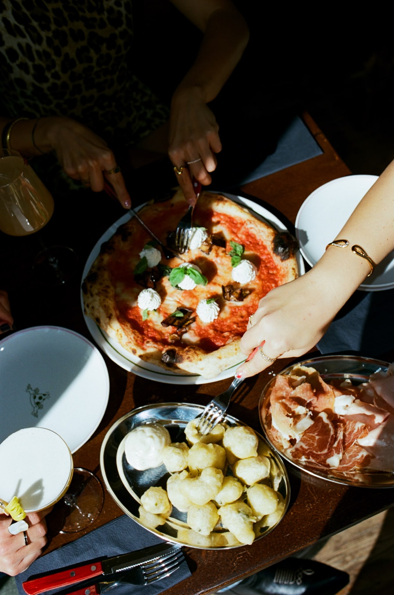 Overhead spread of pizza, frittelle and prosciutto shared among friends