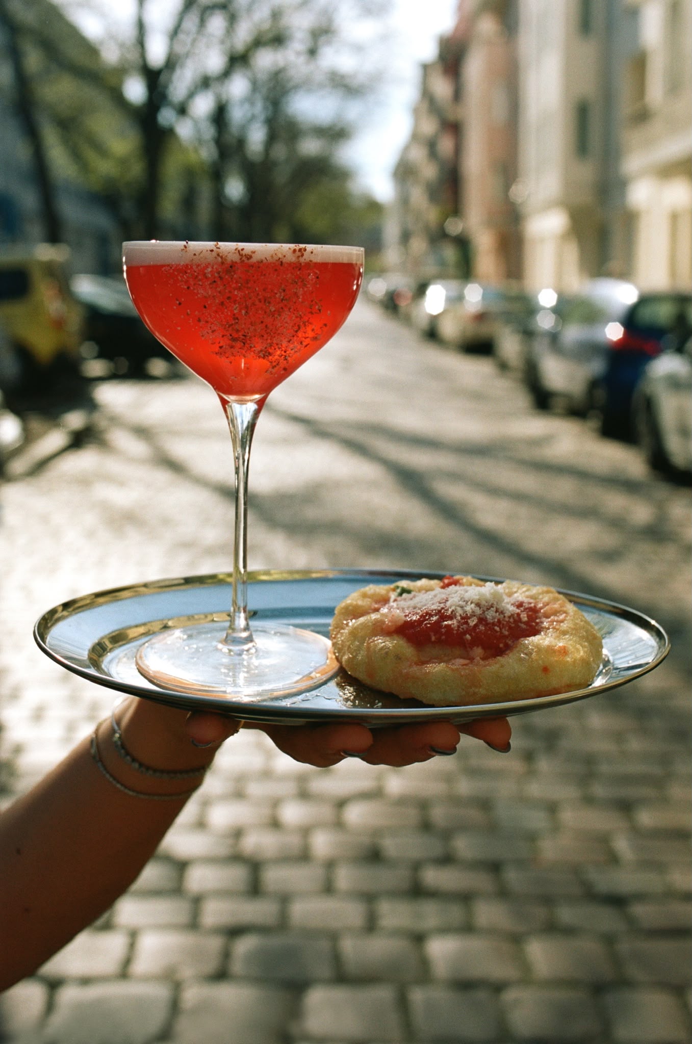 A coupe cocktail and pizzetta served on a Berlin cobblestone street