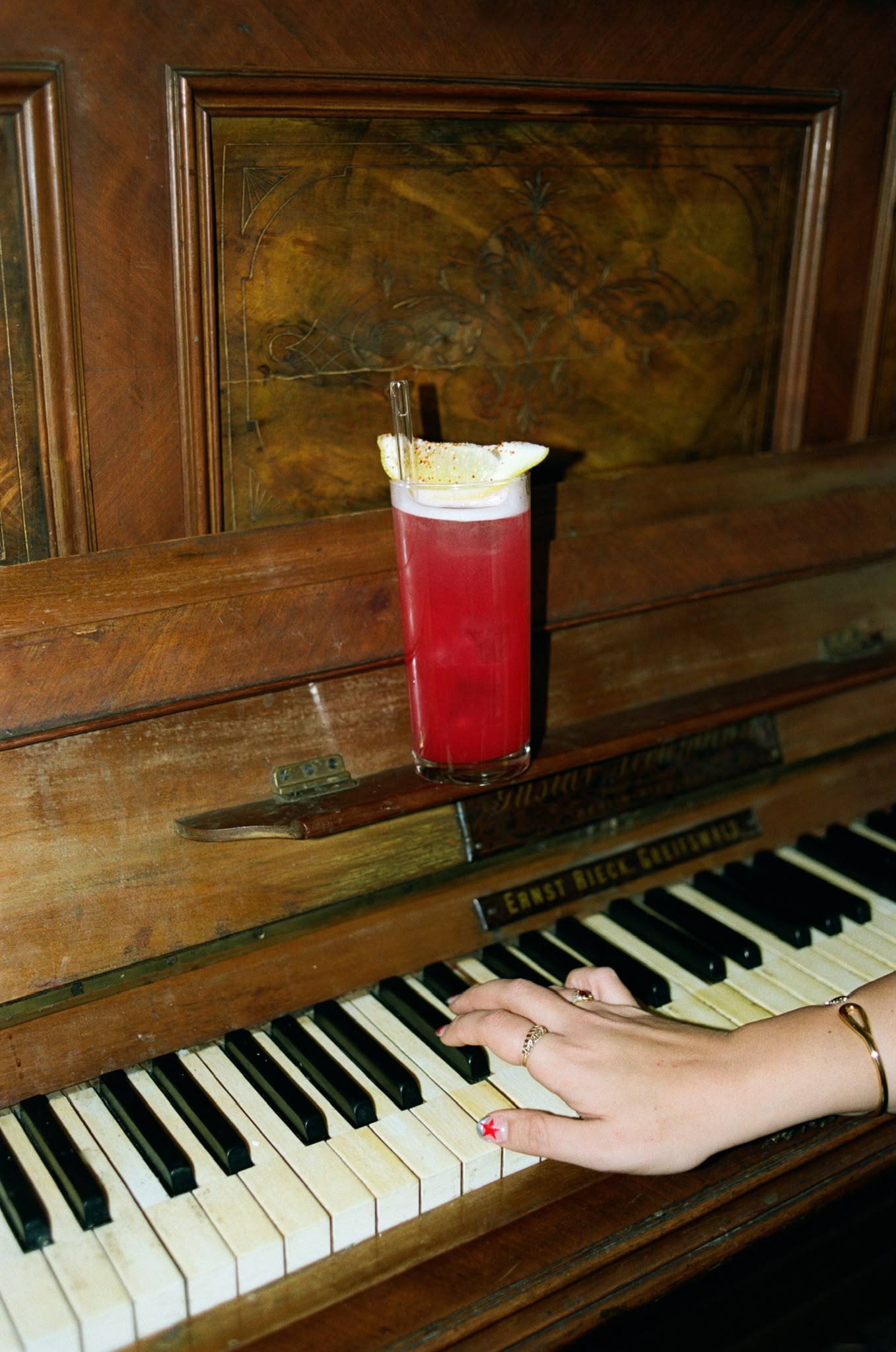 A red cocktail resting on an antique piano