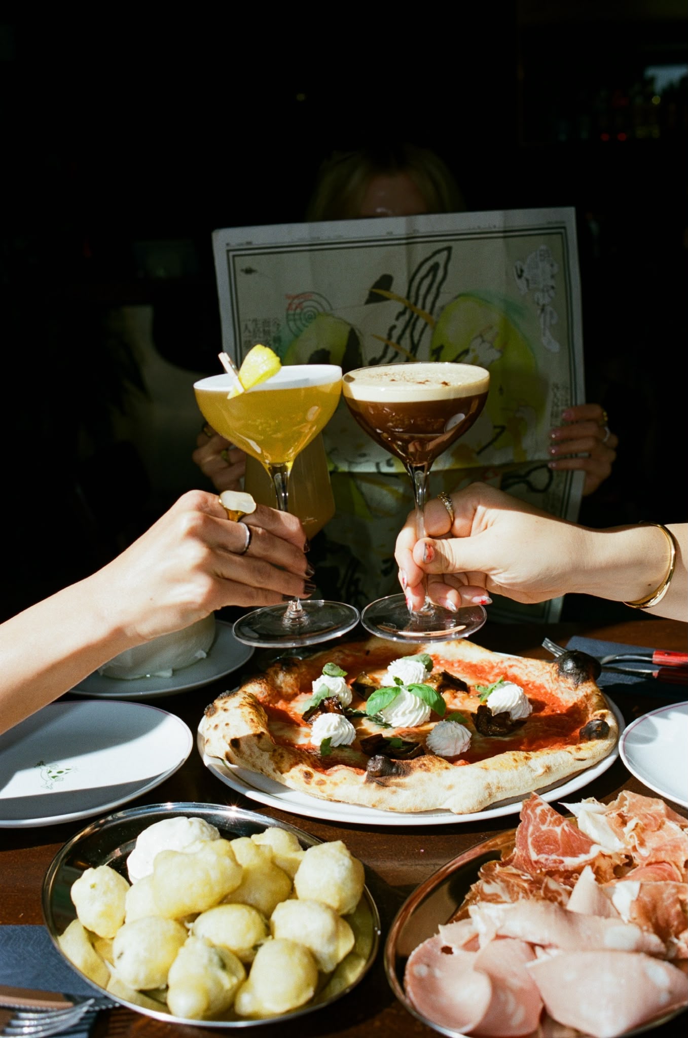 Friends toasting cocktails over a fresh pizza